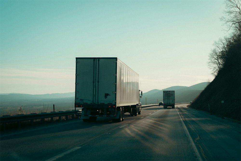 Caminhões seguindo viagem por uma rodovia de serra no fim da tarde